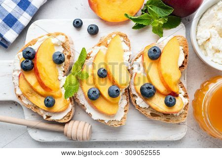 Delicious Toast With Soft Ricotta Cheese, Fresh Juicy Peach, Blueberry And Honey On White Wooden Boa