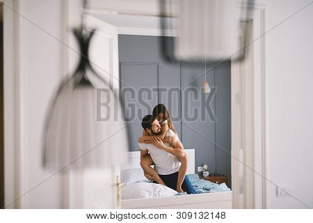 Cute Girl Hugging Bearded Man From Behind While Sitting On The Bed