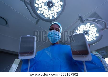 Low angle view of African-american female surgeon using defibrillator in operating room of hospital