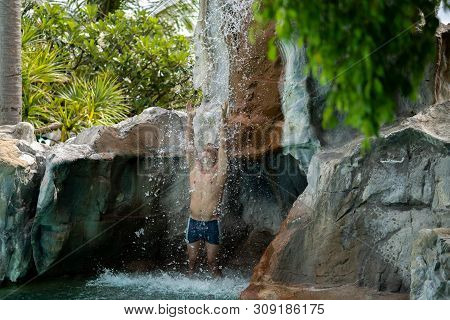 A Young Guy Stands Under Artificial Waterfalls In The Pool On Site
