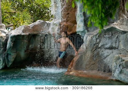 A Young Guy Stands Under Artificial Waterfalls In The Pool On Site