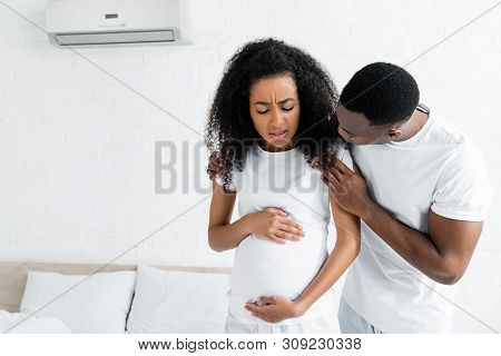 African American Man Hugging Worried And Pregnant Wife In Room