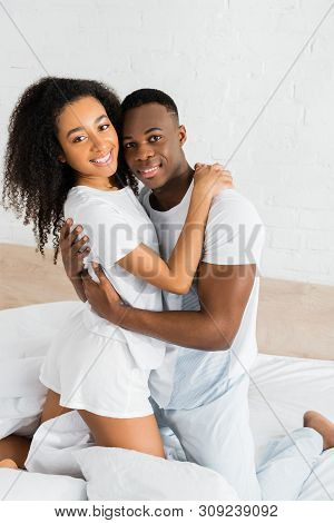 African American Cuople Standing On Bed, Hugging Each Other And Looking At Camera