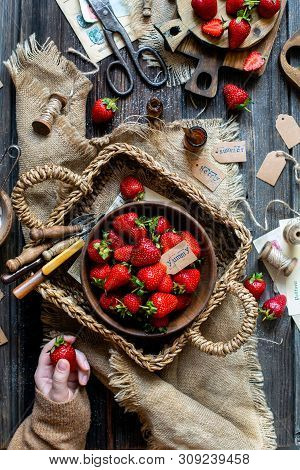 Overhead Shot Of Tasty Ripe Strawberries In Wooden Bowl Stands In Wicker Strawy Basket On Rustic Tab