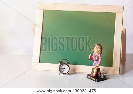 Back To School. Alarm Clock And The Figure Of The Teacher On The Background Of The Blackboard.