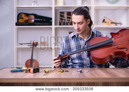 Young handsome repairman repairing violin