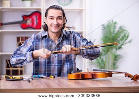 Young handsome repairman repairing violin