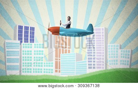 Man In Aviator Helmet Sitting In Propeller Plane And Flying Above Town. Pilot Driving Aeroplane On B
