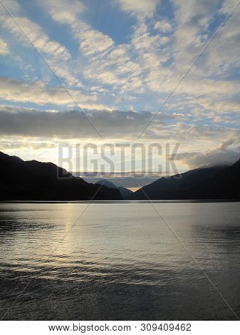 Our Golden Hour With Glowing Clouds In The Sky Reflected In The Lake. The Silhouettes Of The Mountai