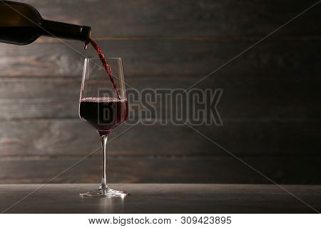 Pouring Red Wine Into Glass From Bottle On Table Against Wooden Background. Space For Text