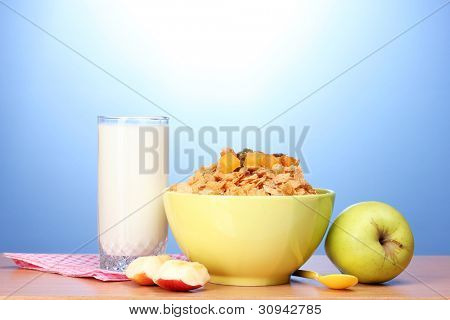 leckere Cornflakes in grüne Schale, Äpfel und Glas Milch auf Holztisch auf blauem Hintergrund