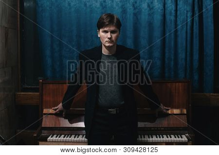 Classical Musician Performer Near Piano. Musical Artist In Dark Room Of Culture House. Portrait Of C