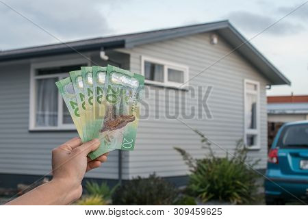 Cropped Shot View Of Men Hand Holding New Zealand Dollar Bills In Front Of A Single House In New Zea