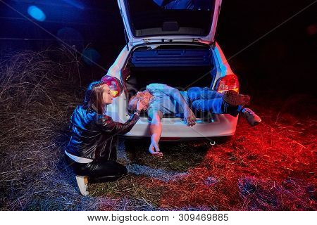 Female Bandit Near The Car And A Dead Or Drunk Guy In The Trunk At Night. Photoshoot About Life Of G