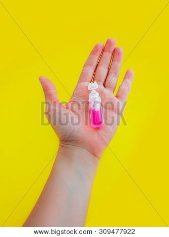 Female Hand Holding One Pink Liquid Medicine In An Ampoule, Isolated On Yellow Background.