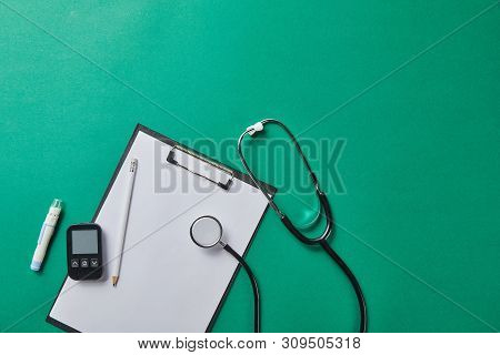 Top View Of Blood Lancet And Stethoscope Near Glucometer And Pencil On Folder On Green Background