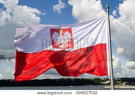 Flag Of Poland. Poland National Flag With Emblem  On Cloudy Blue Sky. Baltic Coast, View From Ship.