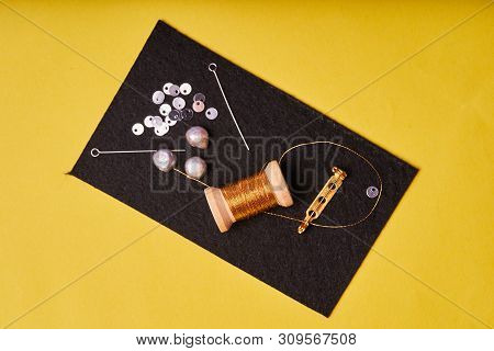 Embroidery Products And Tools. Coil Metal Threads, Pearls And A Pin With The Needle On The Black Fel