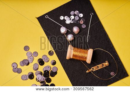 Embroidery Products And Tools. Coil Metal Threads, Pearls And A Pin With The Needle On The Black Fel