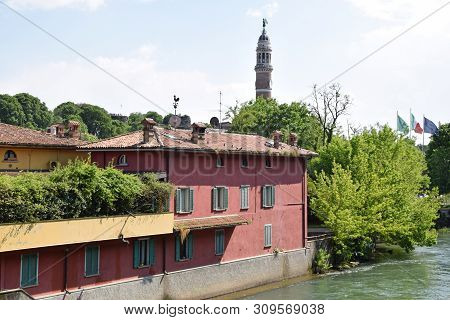 Houses And Buildings On The Oglio River Bank In Palazzolo And In The Background The Tower Of The Peo
