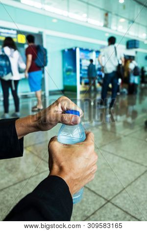 closeup of a young caucasian man opening a bottle of water at the waiting room of a train or bus station, or an airport