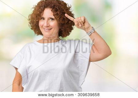 Beautiful middle ager senior woman wearing white t-shirt over isolated background Smiling pointing to head with one finger, great idea or thought, good memory