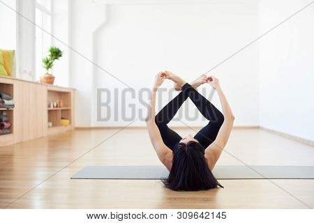 Variation Of Happy Baby Asana. Female Brunette, Invisible Face, Lying Down On Back With Hands And Le