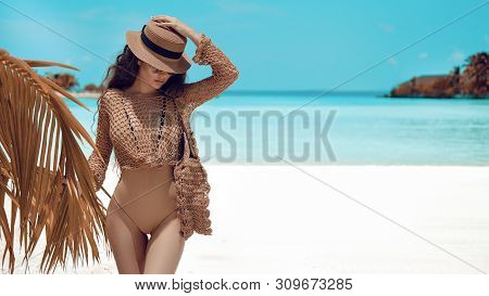 Beautiful Luxury Portrait Of Brunette Woman In Beige Hat, Boho Swimsuit Posing By Ocean Water. Sexy 