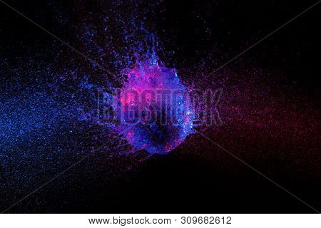 high speed photography. balloon full of water photographed in the exact instant of impact and breaking. blue and purple lights, black background.