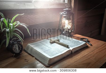 Close Up Christian Cross Putting On Old Bible With Light Of Oil Lamp At Worship Room. Christian Conc