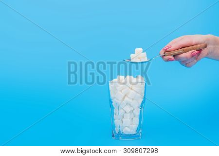 Cropped View Of Woman Holding Teaspoon With Sugar Near Glass With Sugar Cubes Isolated On Blue