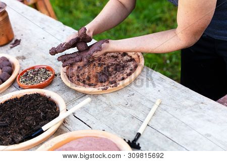 Woman Is Manufacturing Seed Balls Or Seed Bombs On A Wooden Table, Flower Field In The Background