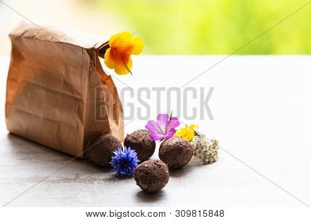 Seed Balls Or Seed Bombs With Various Blossoms On A White, Wooden Background
