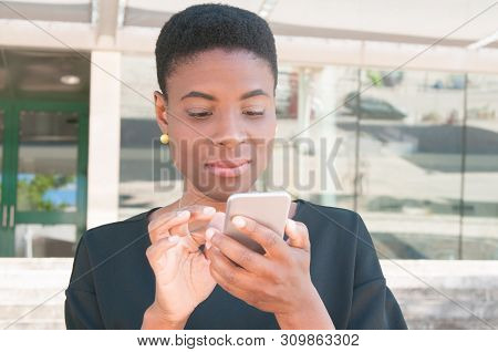 Focused African American Woman Using Online Mobile App. Satisfied Black Lady Holding Using Smartphon