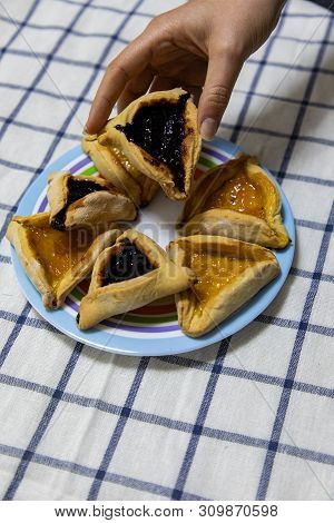 Woman Hand Holding Hamantash Purim Blueberry And Apricot Jam Cookies On Colored Plate On Blue And Wh