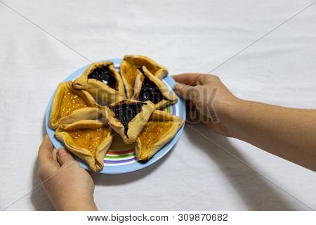 Woman Hands Holding A Colored Plate With Hamantash Purim Blueberry And Apricot Jam Cookies On White