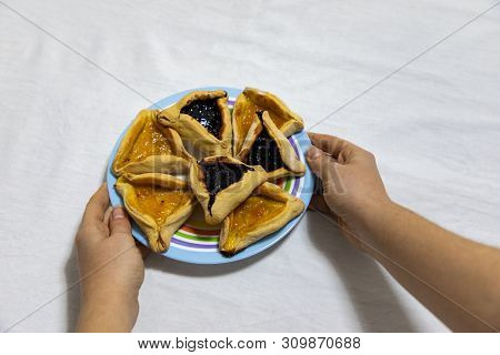 Woman Hands Holding A Colored Plate With Hamantash Purim Blueberry And Apricot Jam Cookies On White