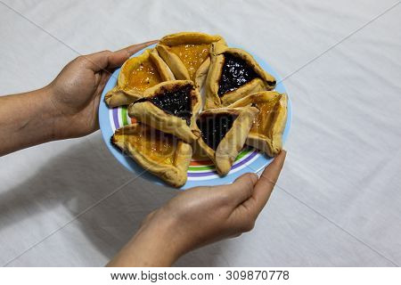 Woman Hands Holding A Colored Plate With Hamantash Purim Blueberry And Apricot Jam Cookies On White