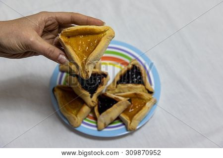 Woman Hand Holding Hamantash Cookie On Top Of Colorful Plate With More Hamantash Cookies