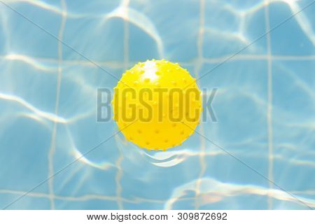 Water Vibrations In The Swimming Pool With Sun Reflection And A Yellow Ball For Playing. Blue Swimmi