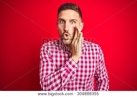Young handsome man over red isolated background hand on mouth telling secret rumor, whispering malicious talk conversation