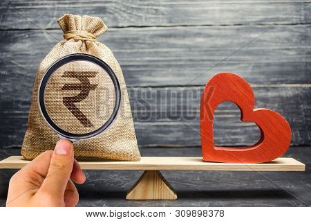 Money Bag With Indian Rupee (rupiah) And Red Wooden Heart On The Scales. Money Versus Love Concept. 
