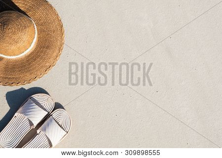 Summer Vacation Concept: Beach Slippers And A Hat On Clean Sand. Top View Of Acessories For Seaside 