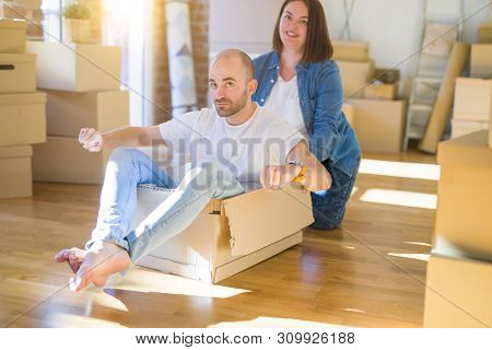 Funny and crazy couple having fun riding a cardboad box as a car, smiling happy and lauging at new home