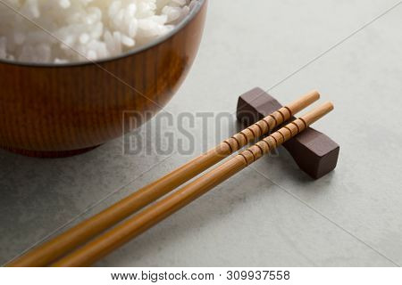 Traditional Japanese wooden chopsticks and a bowl with white rice in the background