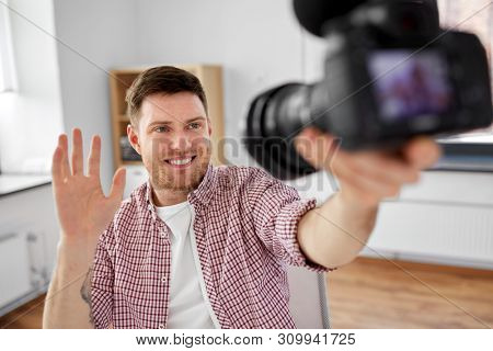 blogging, videoblog and people concept - smiling male video blogger with camera videoblogging and waving hand at home office