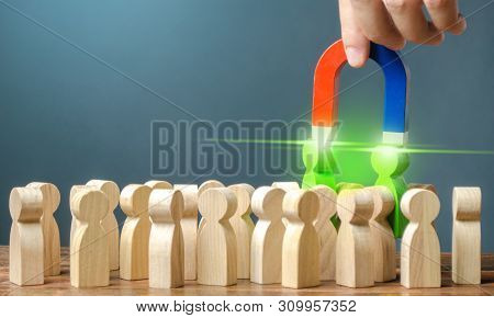 Businessman With A Magnet Pulls Two Green Figures Of People Out Of The Crowd. Recruiting New Workers