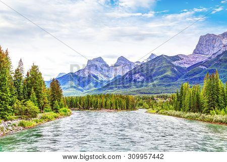 Bow River In Canmore With The Canadian Rockies Mountain Ranges Of The Three Sisters And Ehagay Nakod