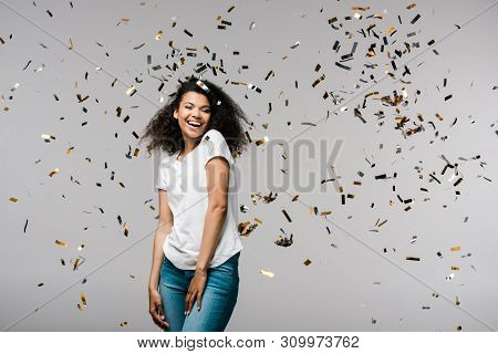 Happy Young African American Woman Smiling Near Shiny Confetti While Standing On Grey