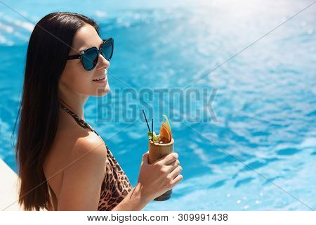 Happy Young Woman In Dark Sunglasses Holding Cocktail While Standing Next To Swimming Pool. Female I